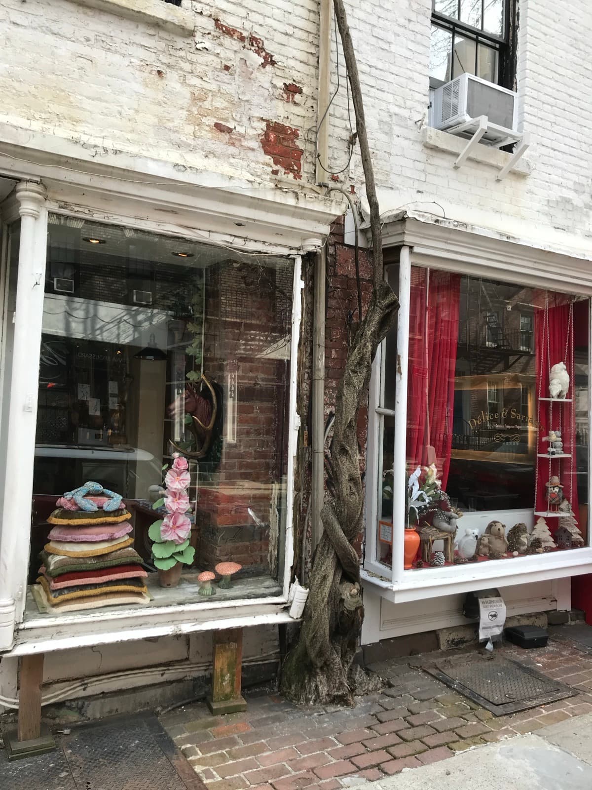 The ground-floor storefronts at 18–20 Christopher Street on March 27, 2019 — white paint peeling down to bare brick around shop windows still filled with sweaters, lamps and curios