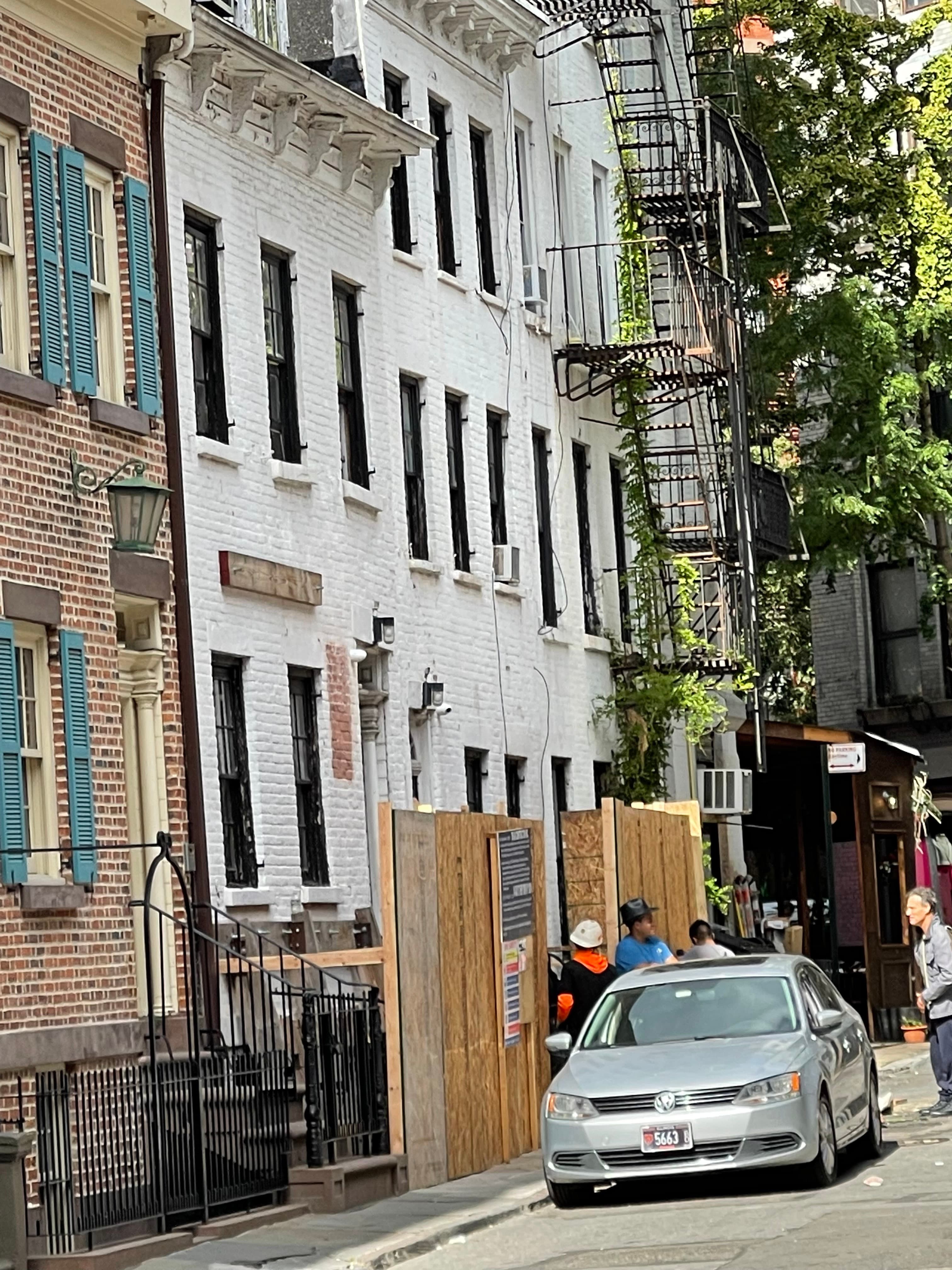 A plywood construction fence with a posted permits panel across the front of the white houses at 14 Gay Street, workers on the sidewalk, September 27, 2022