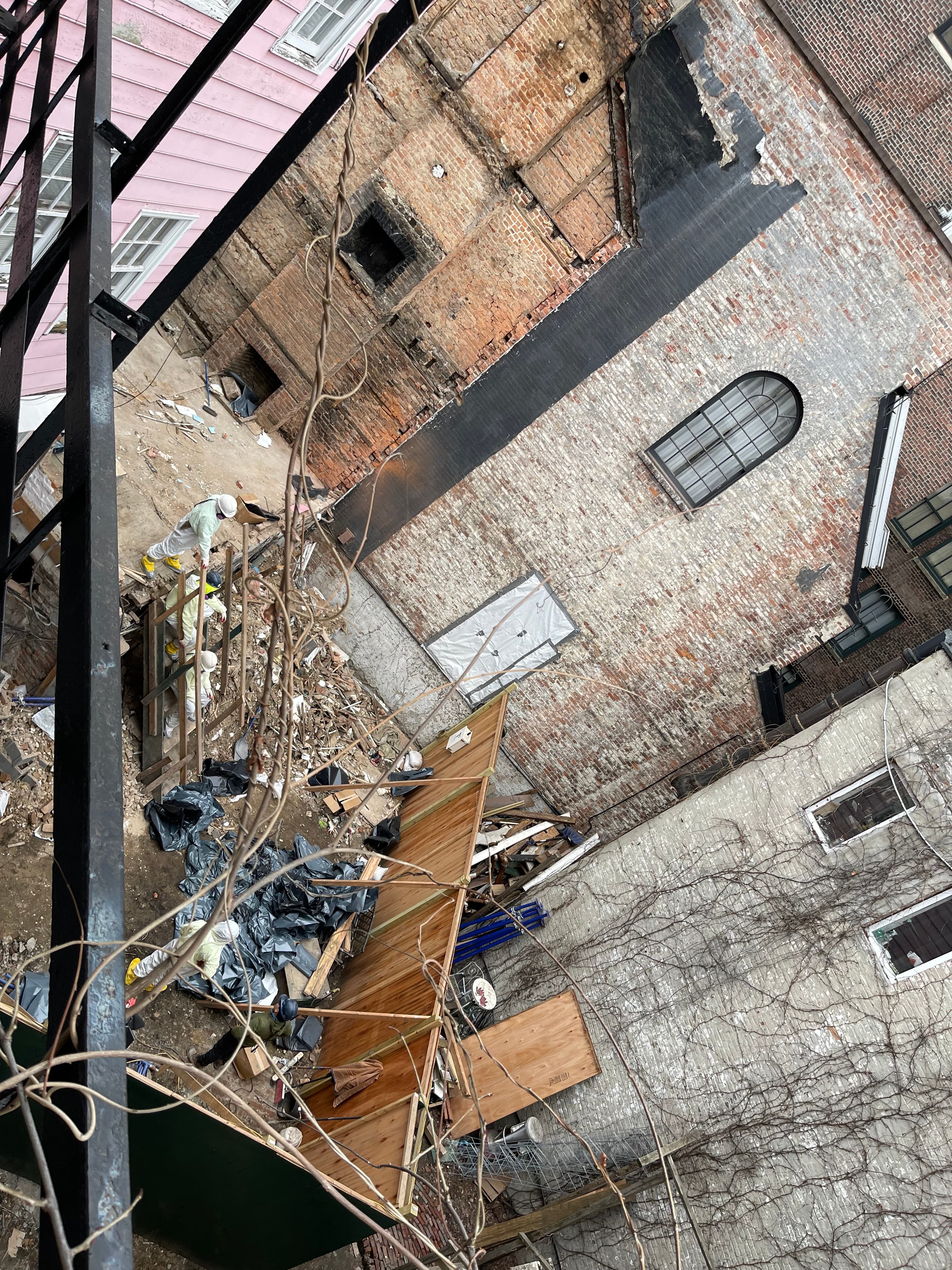 Workers in hazmat suits and yellow boots clearing debris inside the demolished footprint of 14 Gay Street, photographed from above, January 17, 2023