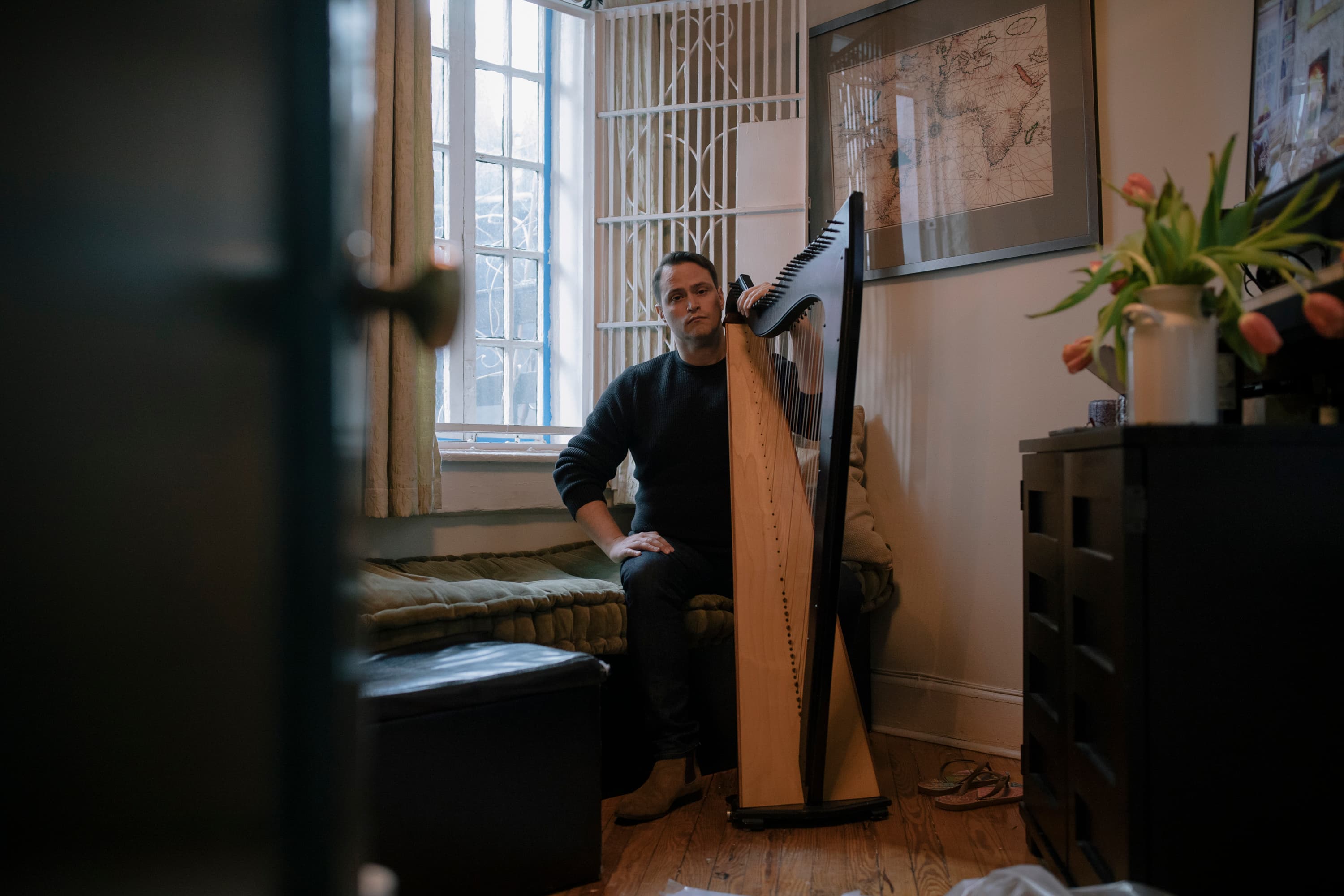 Russell Patrick Brown sits in his 175-square-foot apartment beside his harp, photographed by José A. Alvarado Jr. for Gothamist, February 2023