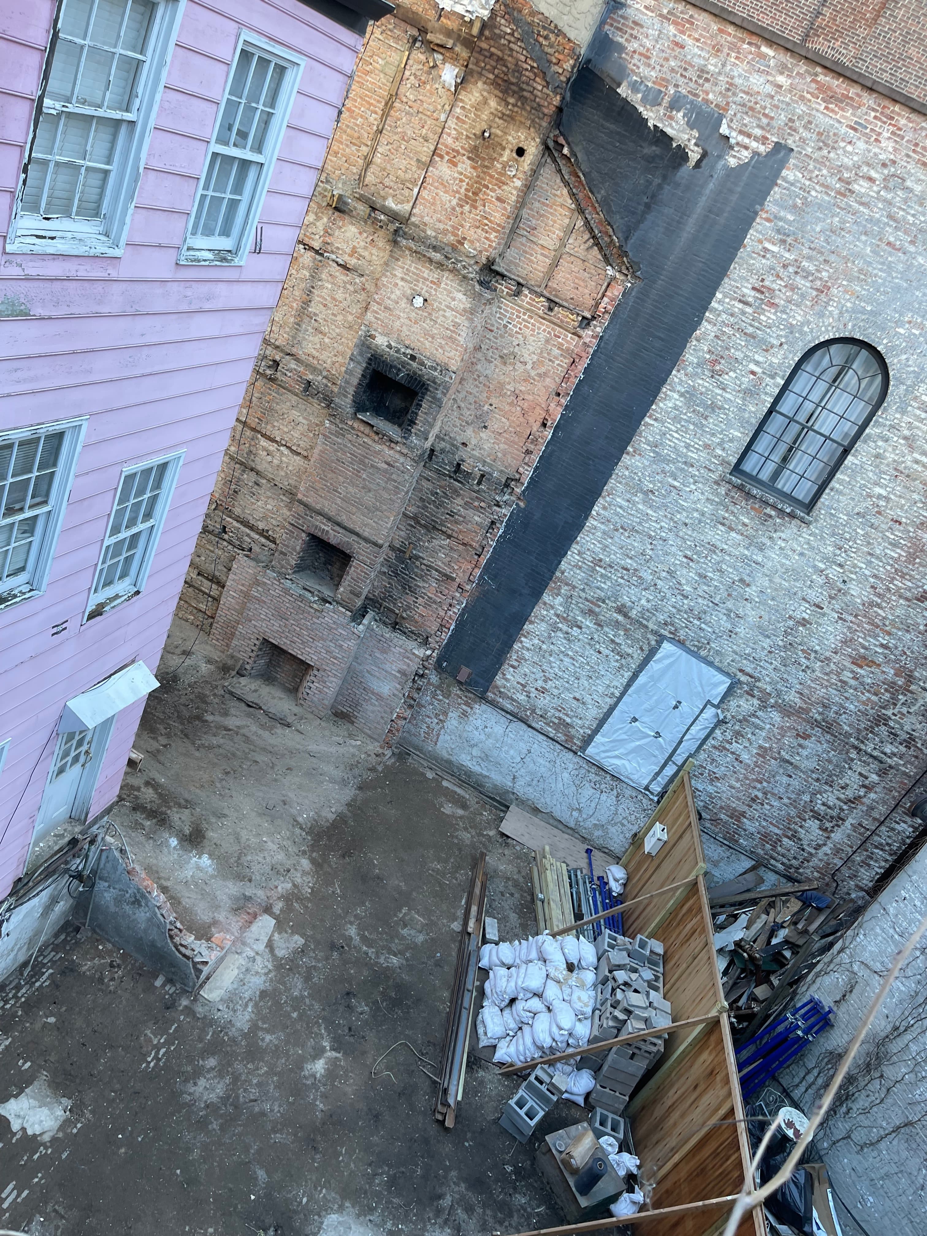 The empty lot where 14 Gay Street stood, photographed February 10, 2023 — the scarred party wall of the neighboring building, a cellar pit, and construction materials