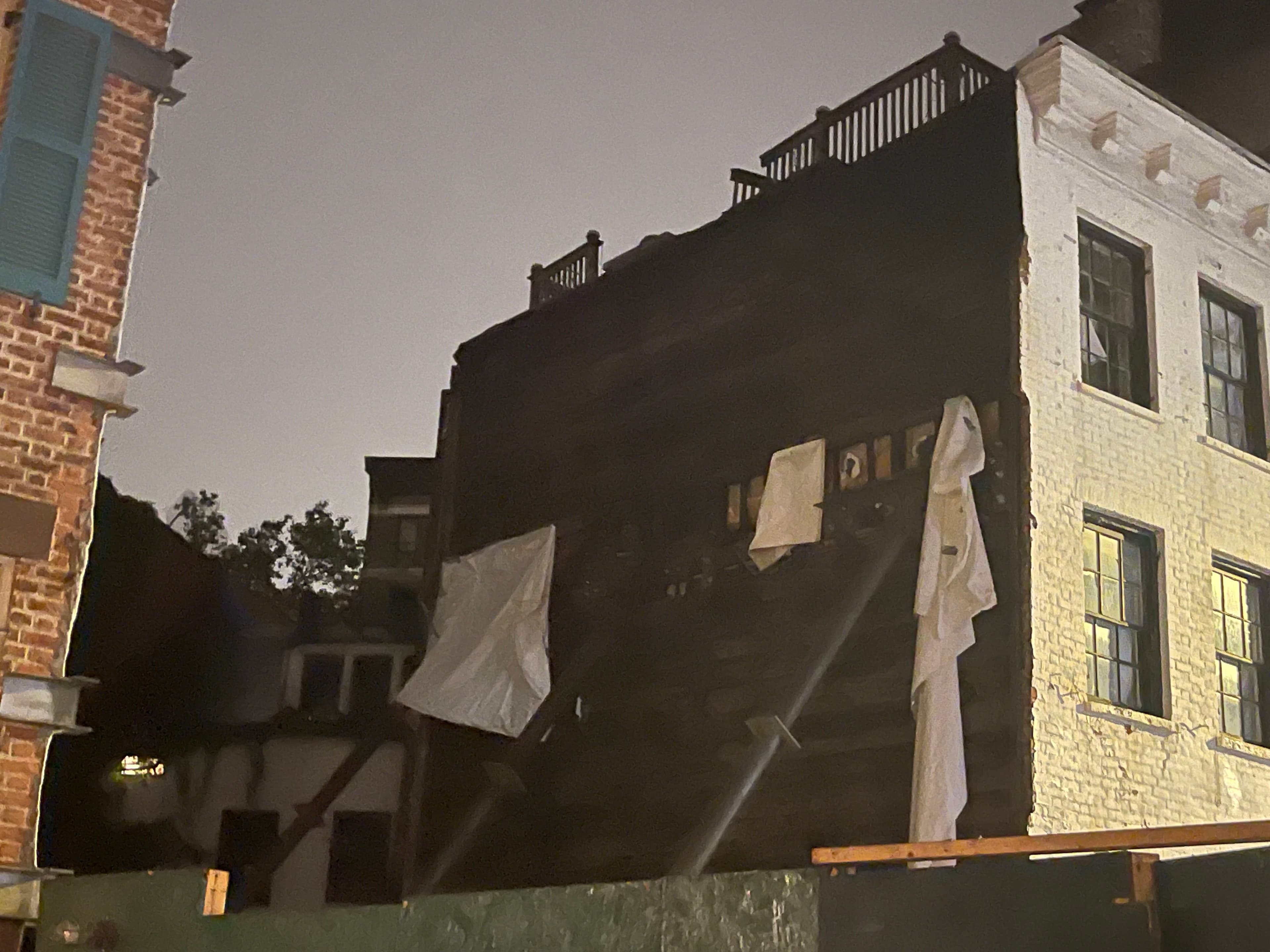 The unprotected party wall of 16 Gay Street at night on May 20, 2023 — loose tarps hanging over the ghost outline of floors and stairs left by the demolished 14 Gay Street