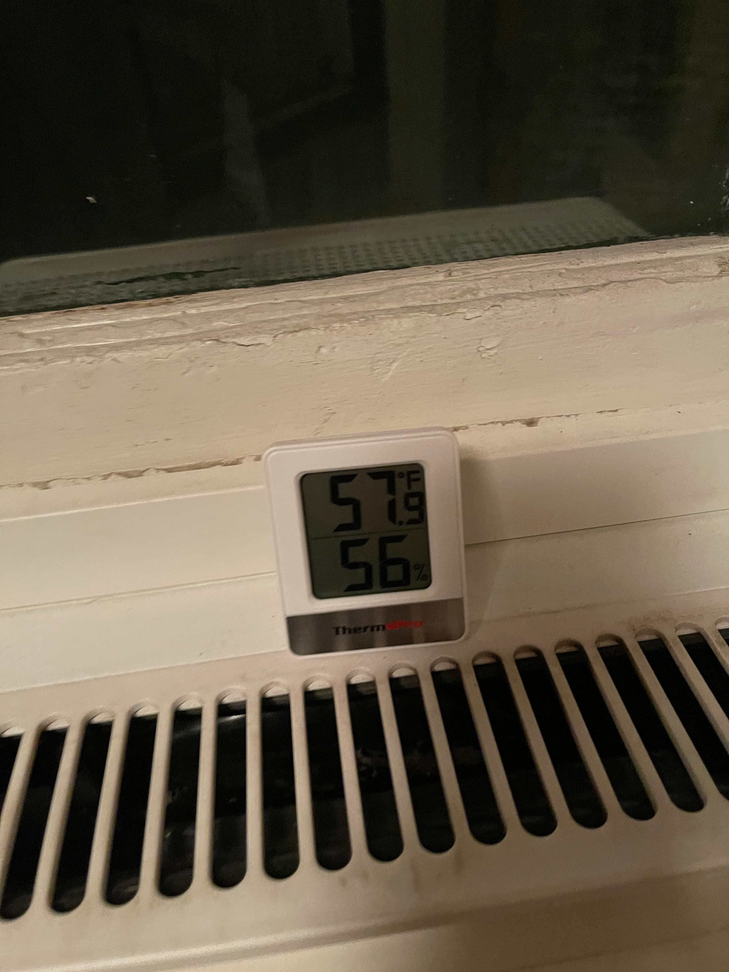 Thermometer showing 64.6°F inside 18 Gay Street on December 2, 2023, with a radiator and peeling paint visible