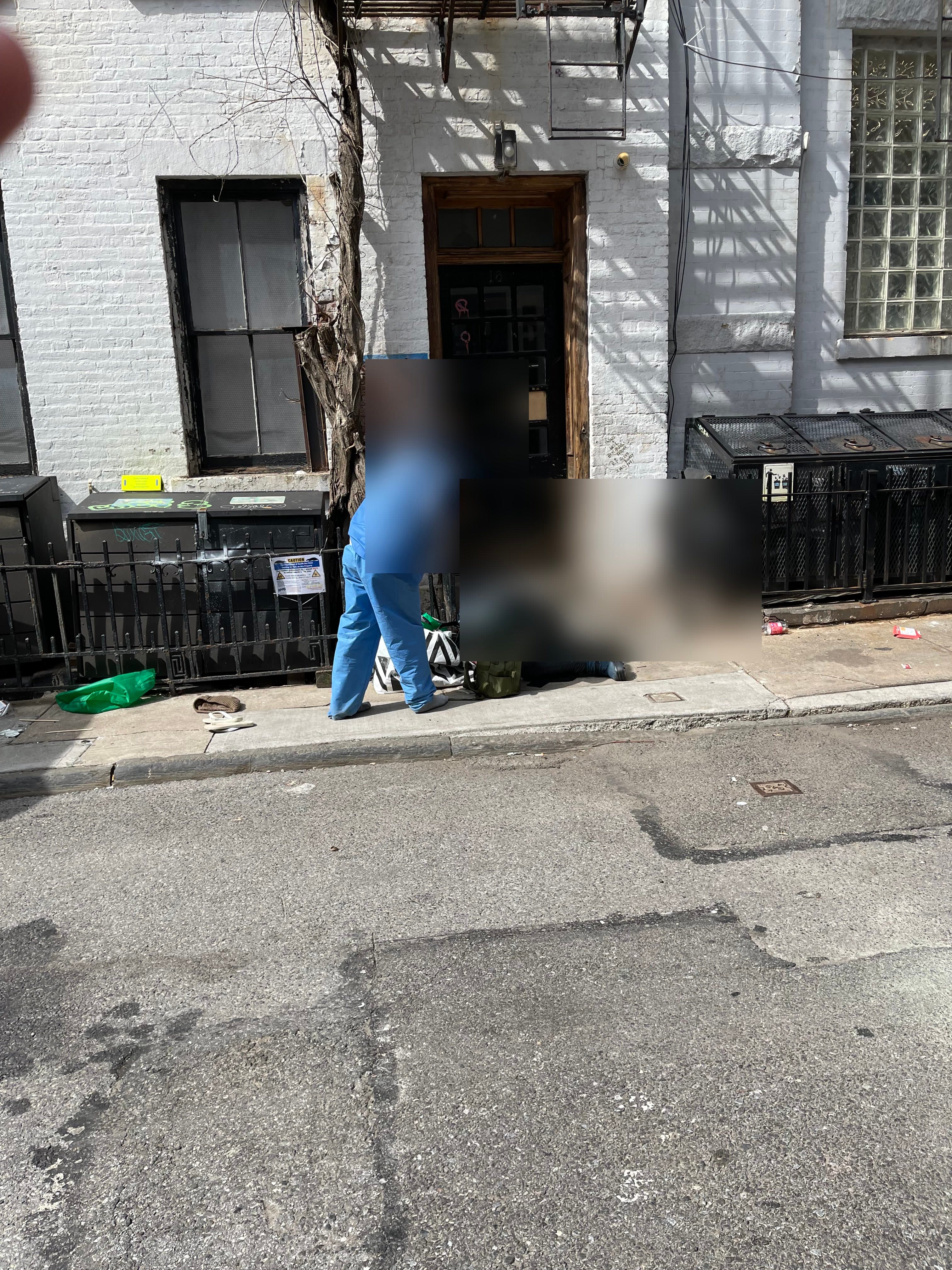 Two people using drugs at the front doorway of 18 Gay Street, their identities obscured, violation notices posted on the railings, March 13, 2024