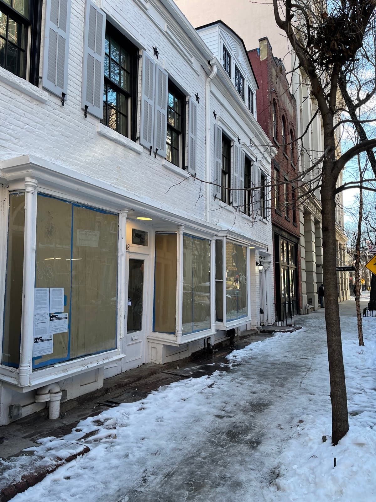 18–20 Christopher Street on February 10, 2025 — the facade repaired and freshly painted white, the storefront windows papered over, an NYC notice posted by the door, snow on the pavement