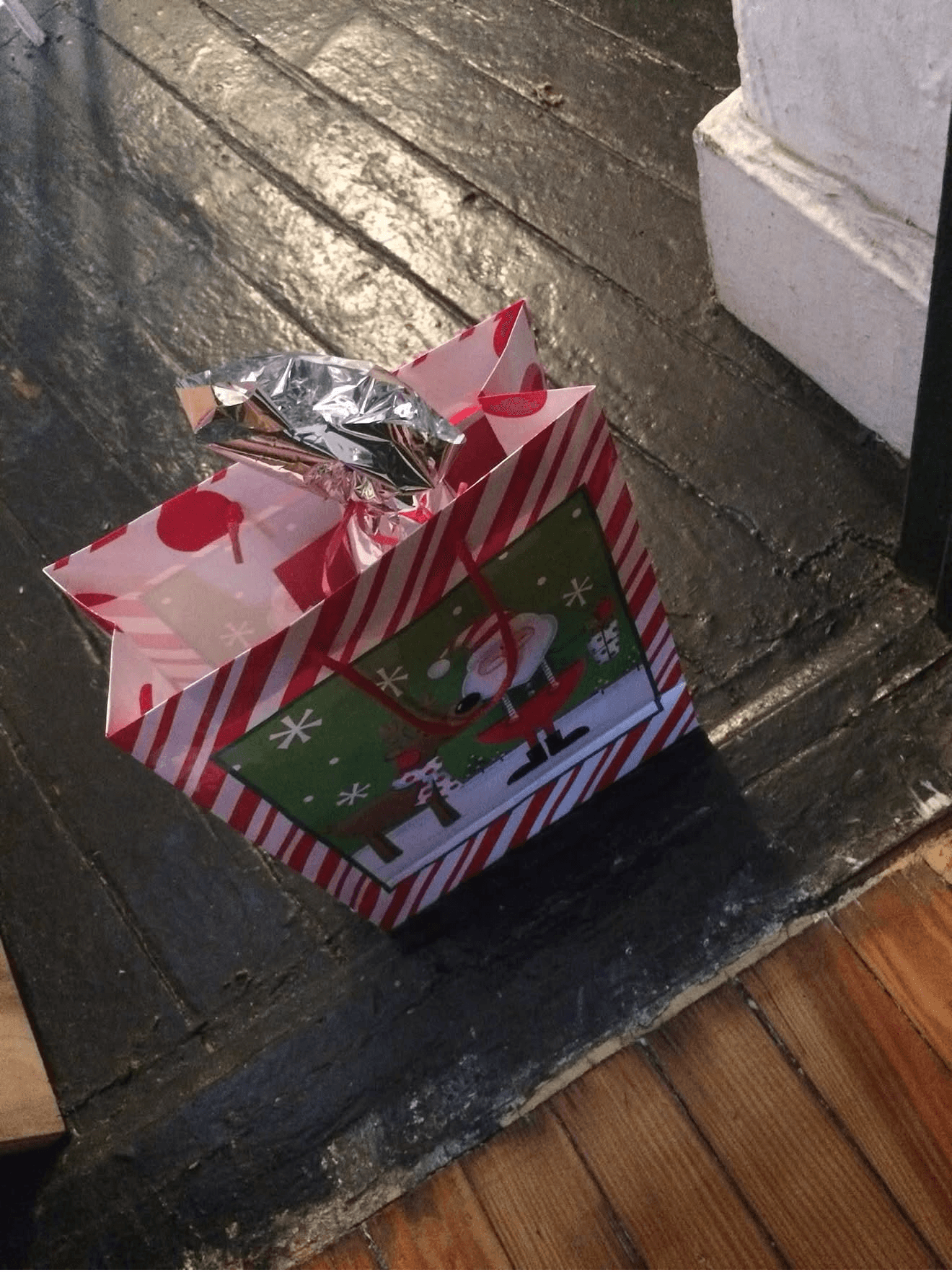 A red-and-white striped Christmas gift bag with a Santa tag and foil tissue, left on the doorstep at 18 Gay Street