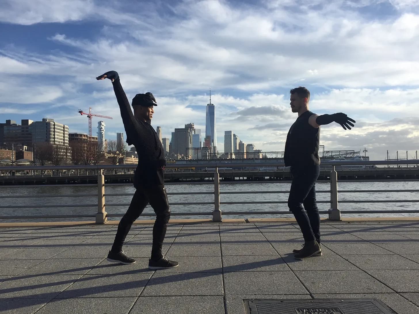 Two dancers facing each other on the Christopher Street Pier, the Manhattan skyline behind them