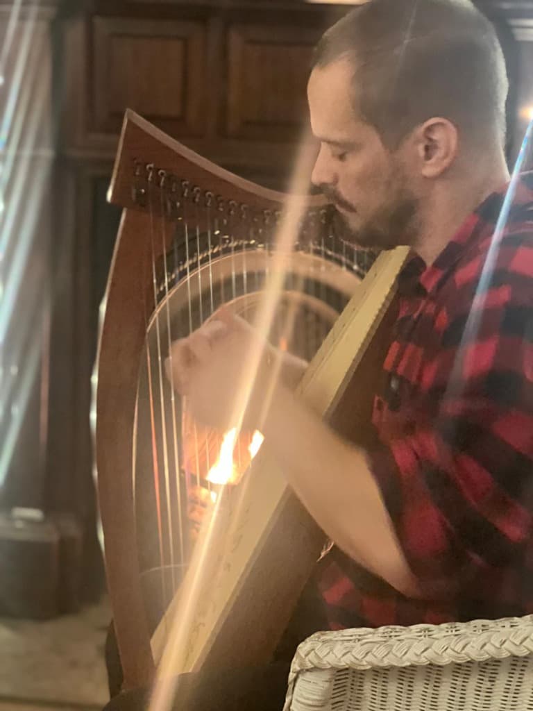 Russell Patrick Brown playing the harp, lit by firelight