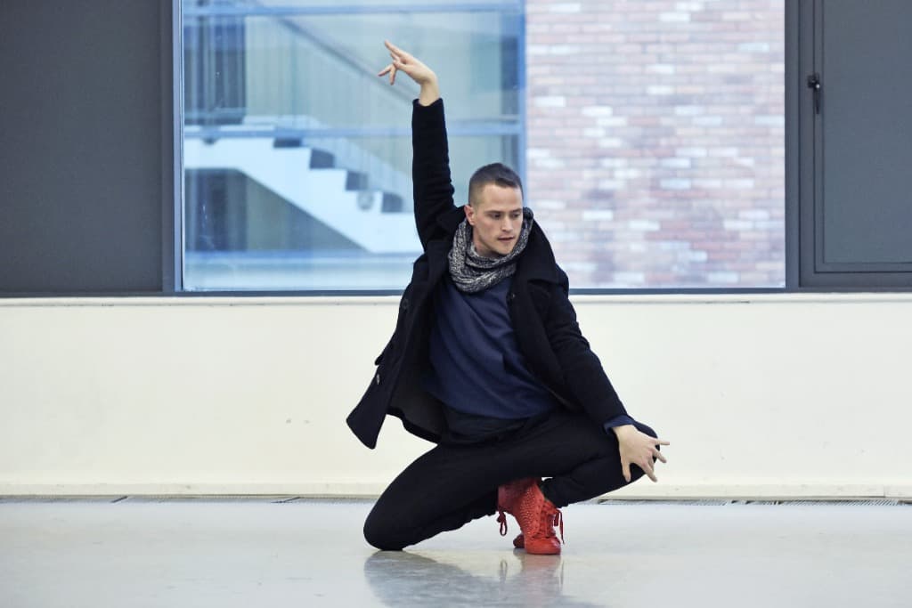 Russell Patrick Brown in a low dance pose in a studio, arm raised